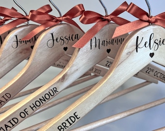 May include: Wooden hangers with names and titles in black script, each topped with a rust-colored ribbon bow. The hangers are personalized with names like "Jessica" and titles like "Bridesmaid". The date "22nd October 2022" is also printed.