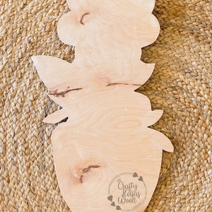 May include: A wooden cutout in the shape of a flower and vase. The natural wood grain is visible. The Crafty Heifas Wood logo is at the bottom. A jute string is attached for hanging.
