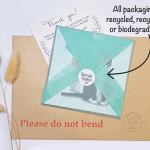 Peut inclure: Une enveloppe en papier brun avec une carte envelopp&eacute;e de papier de soie turquoise &agrave; l'int&eacute;rieur. La carte pr&eacute;sente une illustration en noir et blanc d'un chat. L'enveloppe porte l'inscription "Veuillez ne pas plier" imprim&eacute;e dessus. Le papier de soie porte l'inscription "Georgie Sutton Art" imprim&eacute;e dessus. La carte porte l'inscription "Merci !" imprim&eacute;e dessus. L'enveloppe a un petit autocollant avec le texte "Georgie Sutton Art" imprim&eacute; dessus. Le texte "Tous les emballages sont recycl&eacute;s, recyclables ou biod&eacute;gradables !" est &eacute;crit dans une bulle de dialogue au-dessus de l'enveloppe.