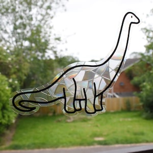 Pode incluir: Um adesivo de dinossauro transparente e iridescente com um padr&atilde;o de mosaico. O dinossauro &eacute; contornado em preto e tem um pesco&ccedil;o e uma cauda longos.