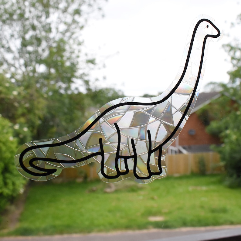 Pode incluir: Um adesivo de dinossauro transparente e iridescente com um padr&atilde;o de mosaico. O dinossauro &eacute; contornado em preto e tem um pesco&ccedil;o e uma cauda longos.