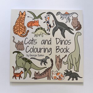 Pu&ograve; includere: Una copertina di un libro da colorare con il titolo "Cats and Dinos Coloring Book" di Georgie Sutton. La copertina presenta illustrazioni di gatti e dinosauri in varie pose, tra cui un grande dinosauro verde con collo lungo, un dinosauro verde pi&ugrave; piccolo con schiena spinosa e una variet&agrave; di gatti con diversi motivi e colori.