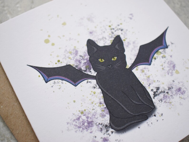 Peut inclure: Un chat noir aux yeux jaunes et des ailes de chauve-souris assis sur un fond blanc avec des &eacute;claboussures d'aquarelle violettes et vertes.