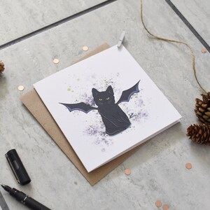 Peut inclure: Une carte blanche avec un chat noir aux ailes violettes sur un fond de peinture &eacute;clabouss&eacute; de violet et de blanc.