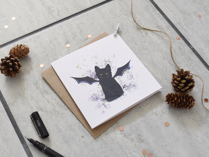 Peut inclure: Une carte blanche avec un chat noir aux ailes violettes sur un fond de peinture &eacute;clabouss&eacute; de violet et de blanc.