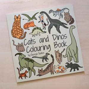 Pu&ograve; includere: Una copertina di un libro da colorare con il titolo "Cats and Dinos Coloring Book" di Georgie Sutton. La copertina presenta illustrazioni di gatti e dinosauri in varie pose, tra cui un grande dinosauro verde, un dinosauro verde pi&ugrave; piccolo, un dinosauro blu e una variet&agrave; di gatti in diversi colori e motivi.