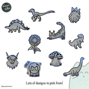 Pode incluir: Uma cole&ccedil;&atilde;o de 10 designs de adesivos diferentes, apresentando v&aacute;rios animais, plantas e objetos. Os designs s&atilde;o delineados em preto e preenchidos com um padr&atilde;o hologr&aacute;fico iridescente azul e verde. Os designs incluem um dinossauro, um gato, um girassol, um cogumelo, uma vaca, um gato em um traje espacial e um dinossauro de pesco&ccedil;o longo.
