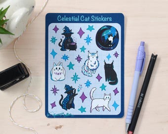 May include: A sheet of stickers featuring celestial cats in various poses, including a cat wearing a witch's hat, a cat with a crescent moon, and a cat with stars. The stickers are on a blue background with a grid pattern. The text "Celestial Cat Stickers" is at the top of the sheet.