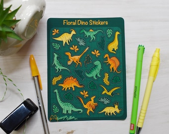 May include: A sheet of green floral dino stickers with a grid pattern. The stickers feature various dinosaurs in orange, yellow, and green colours, with floral and leaf designs. The sheet is labelled "Floral Dino Stickers" and includes the artist's name, "Georgy Sutton Art".