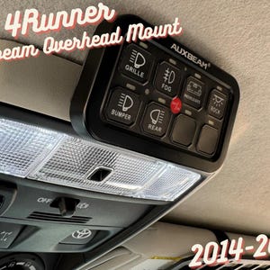 May include: A black AUXBEAM overhead mount switch panel for a 4Runner. The panel has buttons for grille, fog, rock lights, rear, and bumper lights. The text "AUXBEAM" is printed on the panel. The panel is mounted in the overhead console of a 4Runner. The text "2014-2024" is printed on the bottom right of the image.