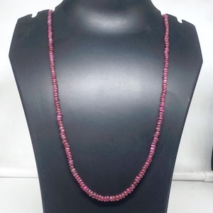 May include: A long necklace of small, round, deep pink beads. The necklace is displayed on a black mannequin, highlighting its length and colour. The beads appear evenly sized and strung together, forming a continuous strand.