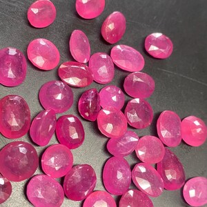 May include: A collection of pink oval-shaped gemstones. The gemstones are faceted and have a shiny, polished finish.
