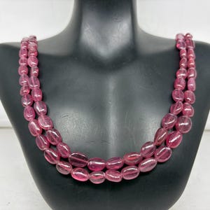 Puede incluir: Un collar de tres hilos con piedras preciosas rosas ovaladas y pulidas. Las cuentas están ensartadas, creando un efecto en capas. El collar se exhibe en un busto de maniquí negro.