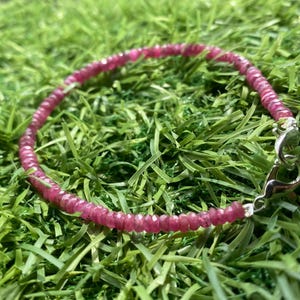 Peut inclure: Un bracelet en pierres précieuses roses avec un fermoir argenté. Le bracelet est composé de petites perles rondes et est posé sur une surface verte.
