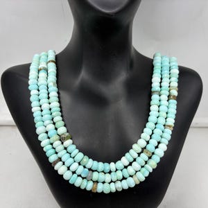 Peut inclure: Collier à plusieurs rangs composé de perles bleu clair et vertes. Le collier est présenté sur un mannequin noir. Les perles ont une forme légèrement irrégulière et sont enfilées pour créer un effet superposé.