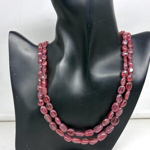 May include: A two-strand necklace of polished, oval-shaped, pink gemstones. The necklace is displayed on a black mannequin bust. The gemstones have a translucent quality, with variations in color from light to deep pink.