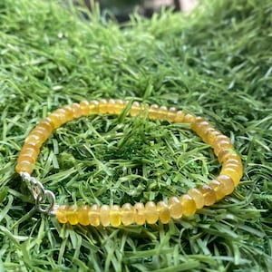 Op de afbeelding: Een gele edelsteen armband met een zilveren sluiting. De armband is gemaakt van ronde kralen en ligt op een groene ondergrond.