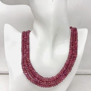 Peut inclure: Un collier à plusieurs rangs composé de petites pierres précieuses rondes, rose foncé. Le collier est présenté sur un buste de mannequin blanc, mettant en valeur le design superposé et la couleur des perles. Les pierres ont un aspect poli.