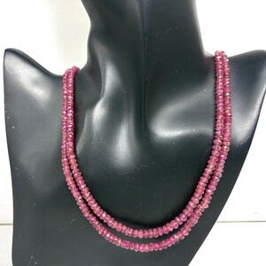 Puede incluir: Un collar de dos hilos con pequeñas gemas rosas facetadas. El collar se exhibe en un busto de maniquí negro. Las gemas tienen una forma ligeramente irregular y un color rosa intenso.