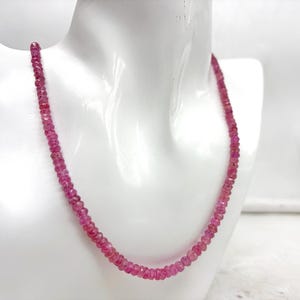 Peut inclure: Un collier de pierres précieuses roses vif présenté sur un mannequin blanc. Le collier est composé de petites perles à facettes, créant un fil continu. Les perles ont une couleur riche et saturée, et le collier est drapé autour du cou du mannequin.