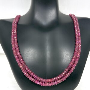 Può includere: Una collana a tre fili composta da piccole pietre preziose rosa sfaccettate. La collana è esposta su un busto di manichino nero. Le pietre preziose hanno una vibrante tonalità rosa-rossastra e le sfaccettature catturano la luce.
