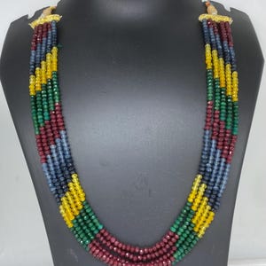 May include: A multi-strand necklace with red, green, blue, and yellow gemstone beads. The necklace is made of faceted beads and has a gold clasp.