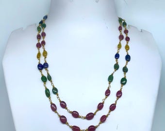 May include: A multi-colored gemstone necklace displayed on a white mannequin. The necklace features oval-shaped gemstones in shades of red, yellow, green, and blue, strung together with gold-colored chain. The necklace is a double strand.