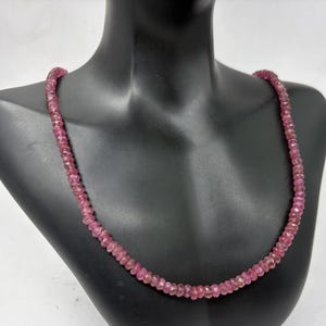 May include: A necklace composed of numerous small, faceted, translucent pinkish-red gemstone beads strung together in a single strand. The beads are uniform in size and shape, creating a continuous circular pattern around the neck area.