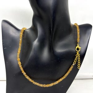 Peut inclure: Un collier composé de petites perles de couleur ambre. Les perles sont enfilées pour former une chaîne délicate. Le collier est présenté sur un mannequin noir. Le fermoir et la chaîne sont de couleur dorée.