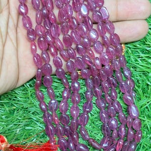 May include: A strand of pink oval-shaped gemstone beads. The beads are translucent and have a slight shimmer. The beads are strung on a clear thread and are approximately 8mm in diameter.