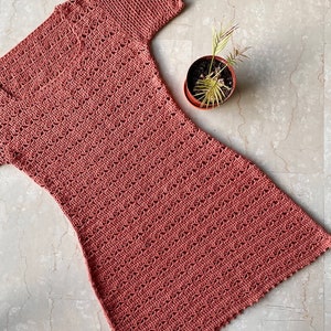 Puede incluir: Un vestido de crochet de color rosa polvoriento con mangas cortas y un dobladillo festoneado.