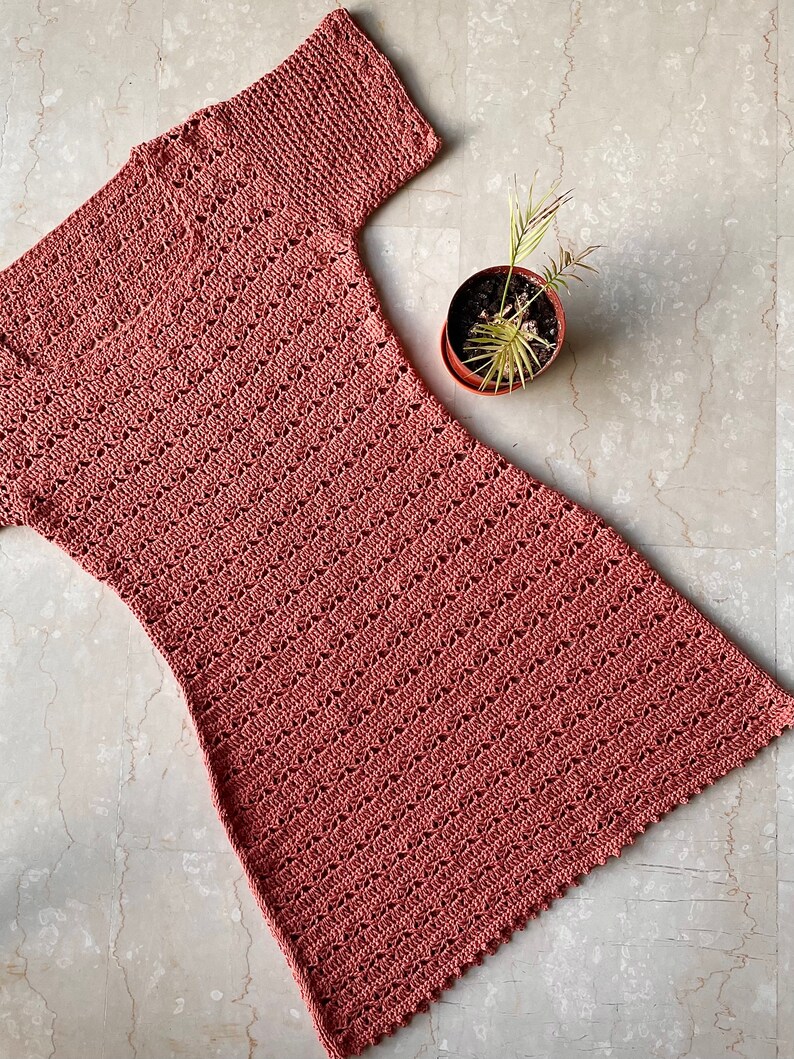 Puede incluir: Un vestido de crochet de color rosa polvoriento con mangas cortas y un dobladillo festoneado.