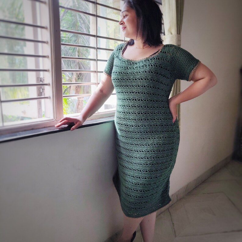 Puede incluir: Una mujer lleva un vestido de crochet verde con cuello redondo y mangas cortas. El vestido tiene un patr&oacute;n de encaje y es ajustado.