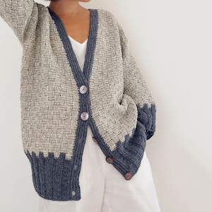 Può includere: Cardigan beige e blu navy con trama intrecciata. Il cardigan ha scollo a V, maniche lunghe e bottoni in legno. Il bordo blu navy accentua i bordi e i polsini.