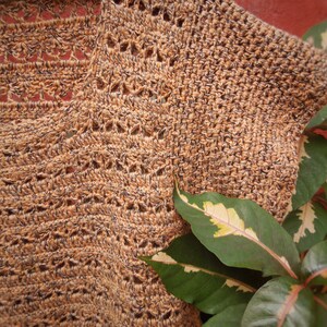 Puede incluir: Primer plano de una tela de crochet marr&oacute;n y negro con un patr&oacute;n texturizado. Una planta verde con variegaci&oacute;n blanca es parcialmente visible en la esquina inferior derecha de la imagen.