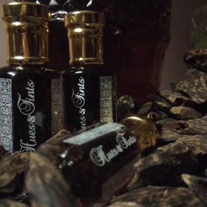 Puede incluir: Tres pequeñas botellas de vidrio con tapas doradas y un líquido oscuro en su interior. Las botellas están etiquetadas con "Hues's Tints". Las botellas están sobre un montón de astillas de madera marrón oscuro.