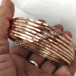 May include: Set of 10 hammered copper bangles. The bangles are stacked on top of each other and are a warm rose gold color.