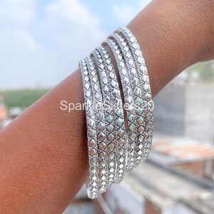 May include: A set of six silver bangles with a geometric diamond pattern. The bangles are stacked on a person's wrist.