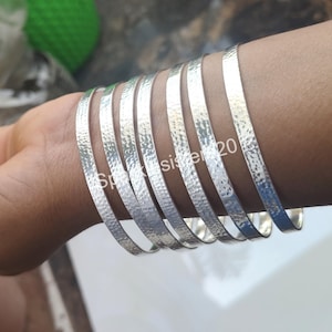 Op de afbeelding: Een set van zeven zilveren armbanden met een gehamerde textuur. De armbanden zijn gestapeld op de arm van een persoon.