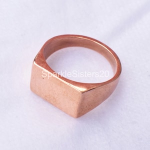 May include: A rose gold signet ring with a square top.