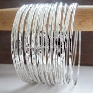 Può includere: Un set di 20 braccialetti in argento martellato. I braccialetti sono impilati uno sopra l'altro e disposti in cerchio.