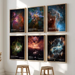 May include: Six framed art prints of nebulae hang on a white wall. The prints feature colorful images of space phenomena, including the Orion Nebula, Mystic Mountain, and Monkey Head Nebula. Two small wooden stools sit below the artwork.