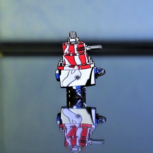 May include: A red, white, and blue fuel pressure regulator pin. The pin is a replica of a fuel pressure regulator and has a small gun on top.