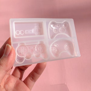 May include: Clear silicone mold with four different video game controller designs. The mold includes a classic NES controller, a Playstation controller, an Xbox controller, and a Sega Genesis controller.