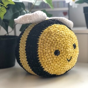 May include: A crocheted plush bee toy with black and yellow stripes, white wings, and black eyes. The bee has a smiling face.