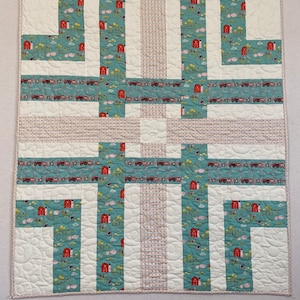 May include: A white and blue patchwork quilt with a farm animal print. The quilt is made up of squares and rectangles of different sizes and colors. The quilt is edged with a white trim.