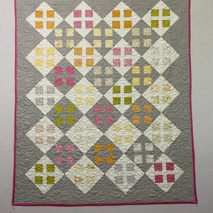 May include: A gray and white quilt with a diamond pattern. The quilt is made with different colored fabrics, including pink, yellow, green, and orange. The quilt is edged with a pink border.