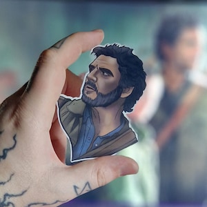 May include: A sticker of a man with a beard and brown hair wearing a brown jacket and a blue shirt. He is looking up and to the right.