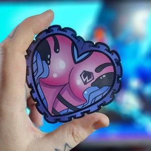 May include: A pink and blue heart-shaped sticker with a black outline and a white letter W inside. The sticker has a detailed design with a wavy pattern.