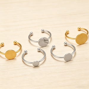 May include: Five open-style rings with a minimalist design. Two are gold-toned, and three are silver-toned. Each ring features a small, flat, circular plate at the center and a small ball at each end of the open band.